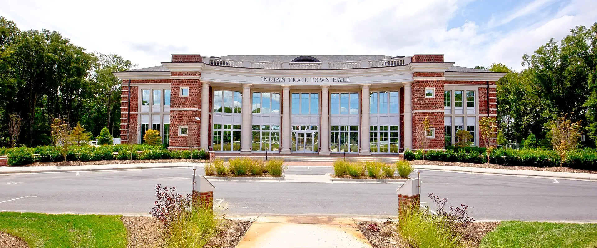 Indian Trail Town Hall, a two-story brick building with white columns and tall windows, under a bright summer sky